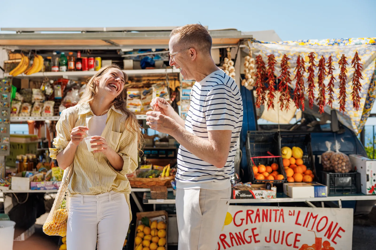 Lachen mit Granita in der Hand an einem bunten Obststand am Straßenrand