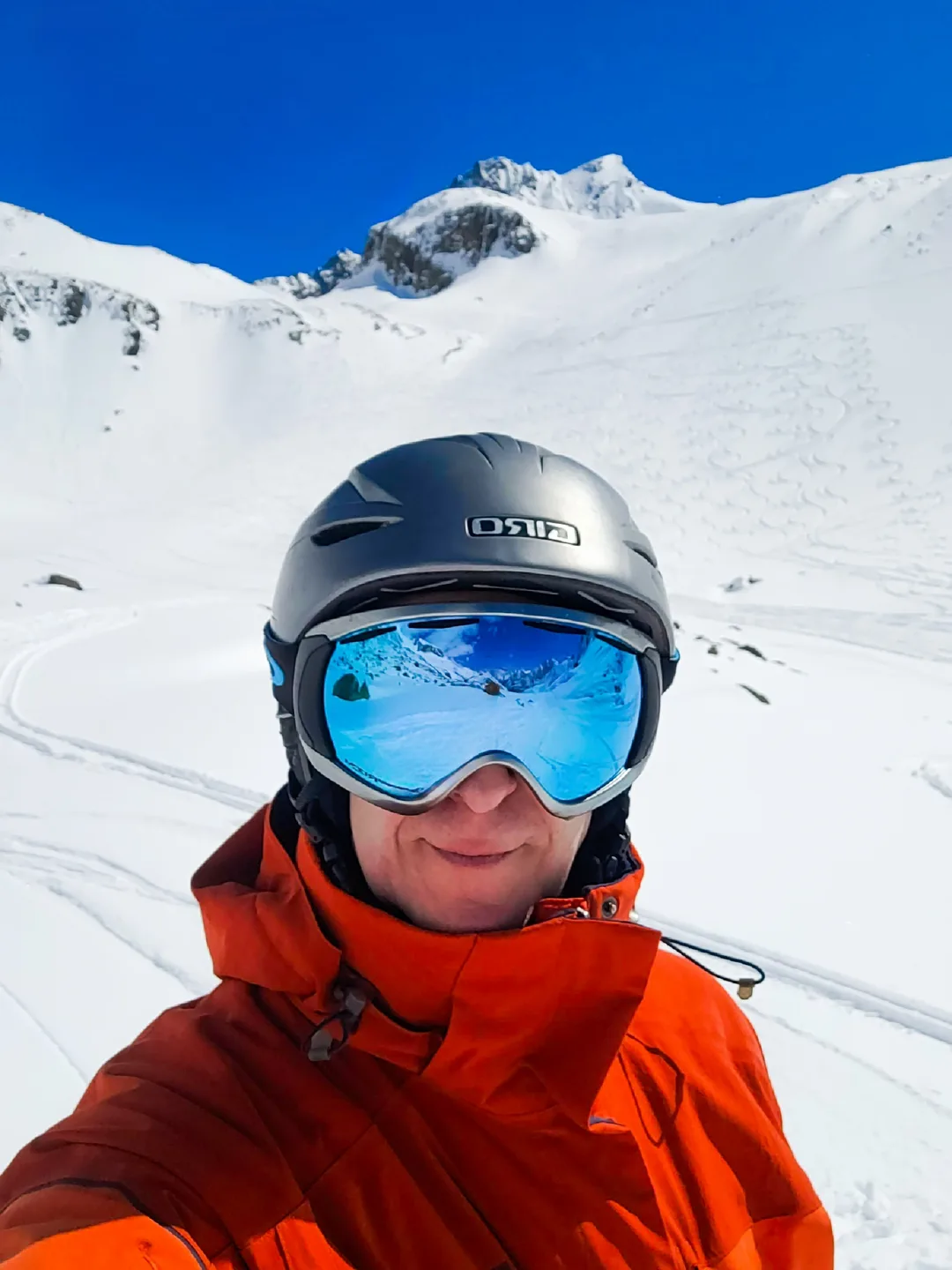 Mit Helm und Snowboardbrille vor einem unverspurten, tiefverschneiten Gipfel