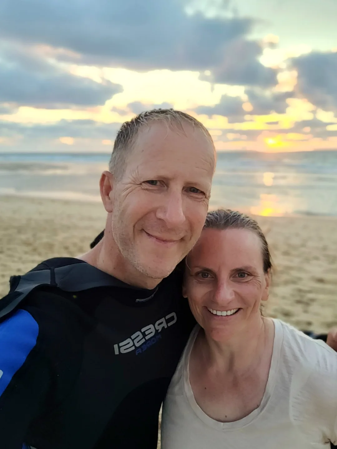 Selfie zu zweit am Strand, hinter ihnen geht die Sonne über dem Meer unter